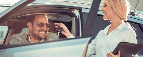 Verkäuferin übergibt dem Käufer einen Autoschlüssel