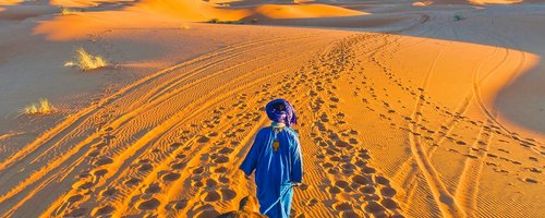 Berber walking with camel at Erg Chebbi orange dunes, Morocco