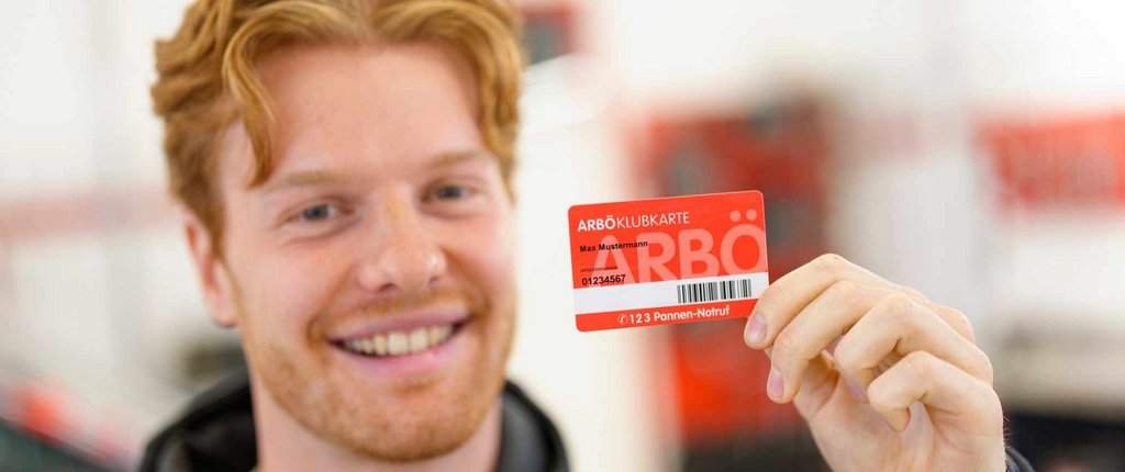 Junger, freundlich lächelnder Mann hält seine ARBÖ-Klubkarte in die Kamera. 