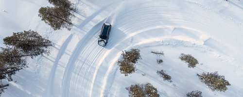 Testfahrzeug fährt in einer Linkskurve auf Schneefahrbahn - Vogelperspektive aufgenommen von einer Drohne