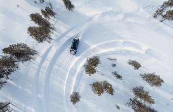 Testfahrzeug fährt in einer Linkskurve auf Schneefahrbahn - Vogelperspektive aufgenommen von einer Drohne