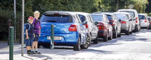2 Kinder stehen am Gehsteig vor einem Zebrastreifen.