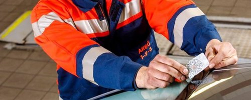 ARBÖ-Techniker klebt Pickerl auf die Windschutzscheibe.