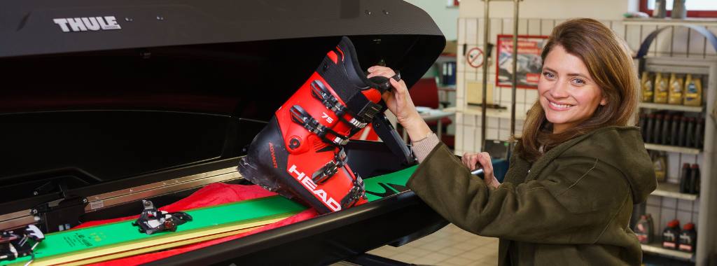 Junge Frau lädt Schischuhe in eine Dachbox.
