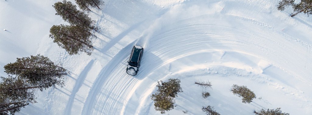 Testfahrzeug fährt in einer Linkskurve auf Schneefahrbahn - Vogelperspektive aufgenommen von einer Drohne